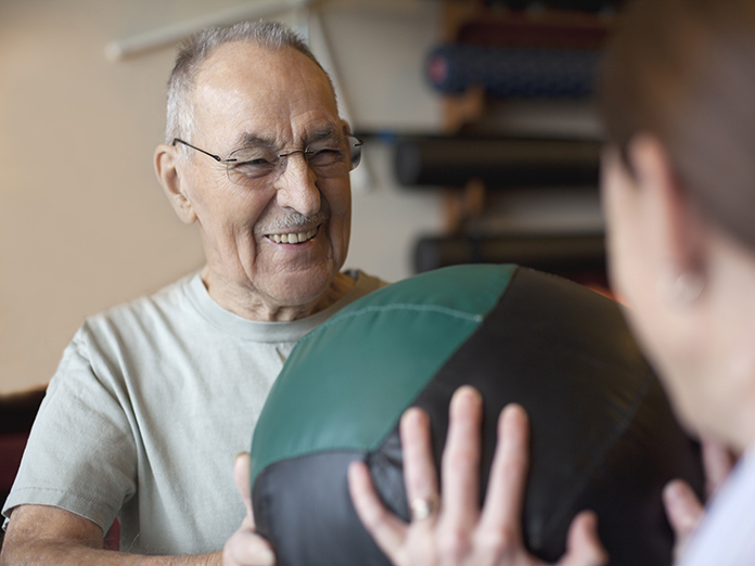 A person holding a medicine ball, working out with their trainer